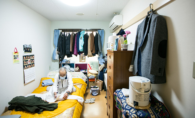 自立支援住宅の部屋の中で服をたたむ男性