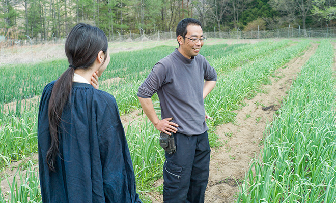 にんにく畑を見ながら笑顔で話す内藤光さんとその話を聞く長田佳子さん