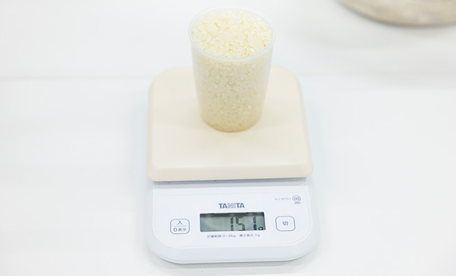 すりきり一杯（約150g）の米を入れた計量カップをのせた電子スケール
