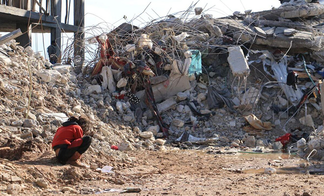 シリア北西部、倒壊した自宅の傍らでしゃがみこむ少女