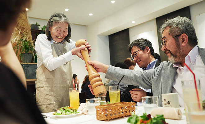 注文をまちがえる料理店の開催時の様子。認知症のスタッフがお客さんの机の料理にこしょうをかけてサービスをしているシーン