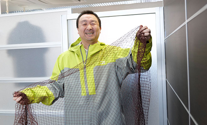 漁網と漁網のリサイクル繊維で作ったカッパを着る長谷川さん