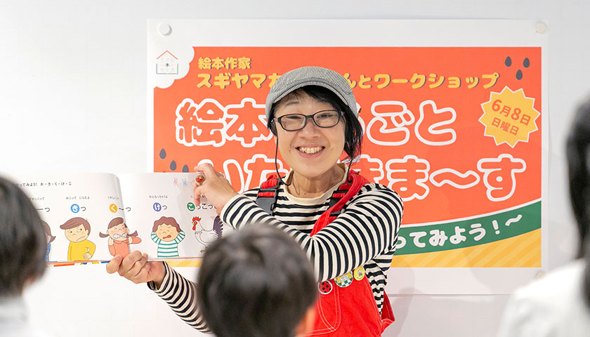 ワークショップで『こえで からだで ゆびもじで やってみよう！あいうえお』（赤ちゃんとママ社、スギヤマカナヨ/作、2024年）を子どもたちと読むスギヤマカナヨさんの画像