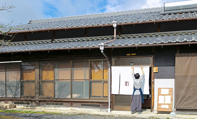 「みかざき麹屋」の店舗の玄関にのれんをかける和田さん