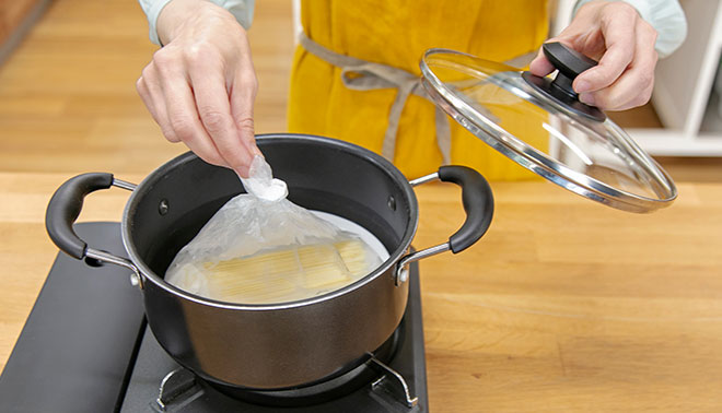 ポリ袋の中にパスタを入れて湯せん調理している場面