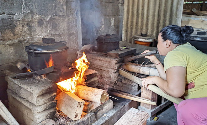 インドネシアバリの朝食準備風景。大きなかまどの前で火を起こして料理をしている女性の画像
