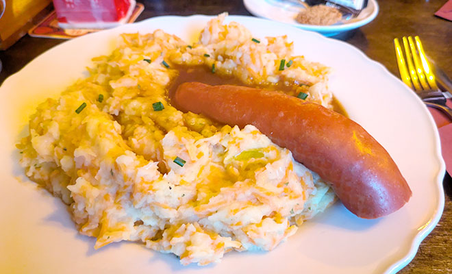 じゃがいもとケールのような青菜を鍋でゆでてつぶした真ssっ湯ポテトの上にウインナーがのったオランダのスタムポットの画像