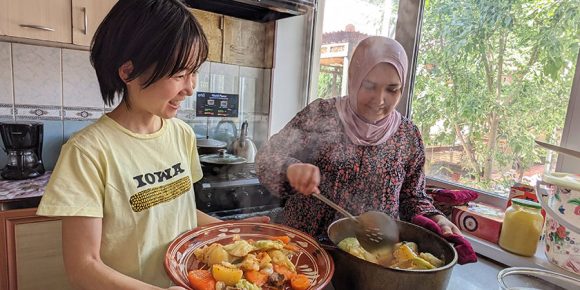 海外の食卓で現地の人と一緒に料理をする岡根谷さん