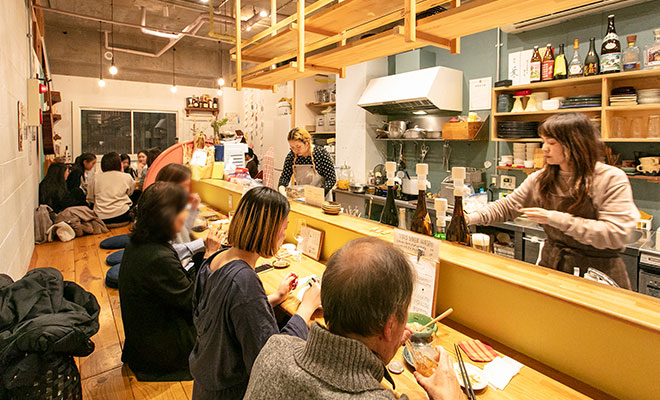 夜の酒場のようす。カウンターは満席で、大人たちがお酒を飲んでいる