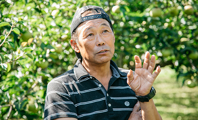 りんご畑で片桐完一さんが真剣な表情で話す